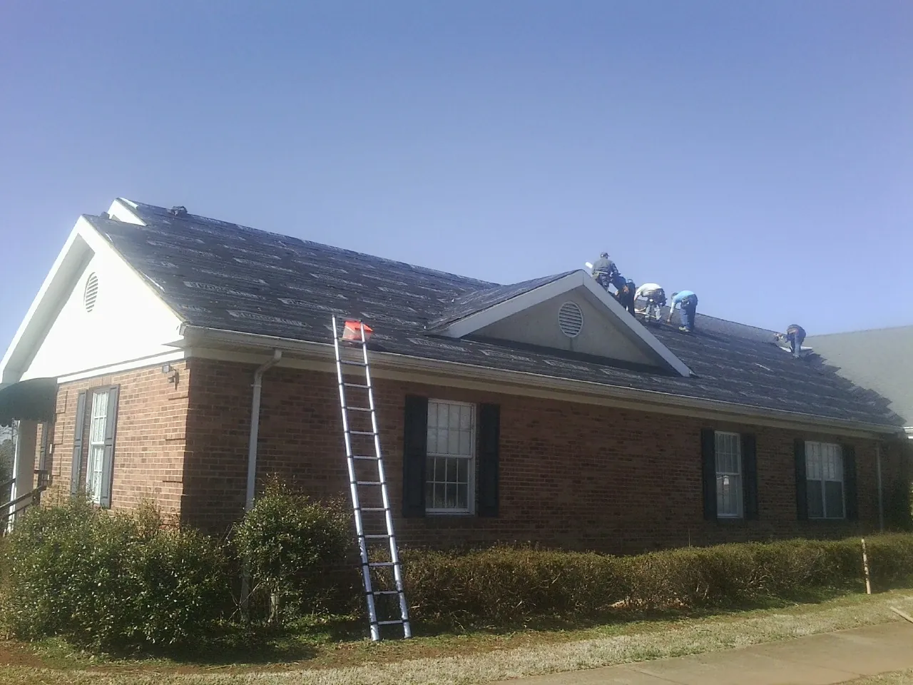 Crew tearing shingles off a brick ranch roof with a ladder set — Emergency Roof Repair work by our crew in Lacygne