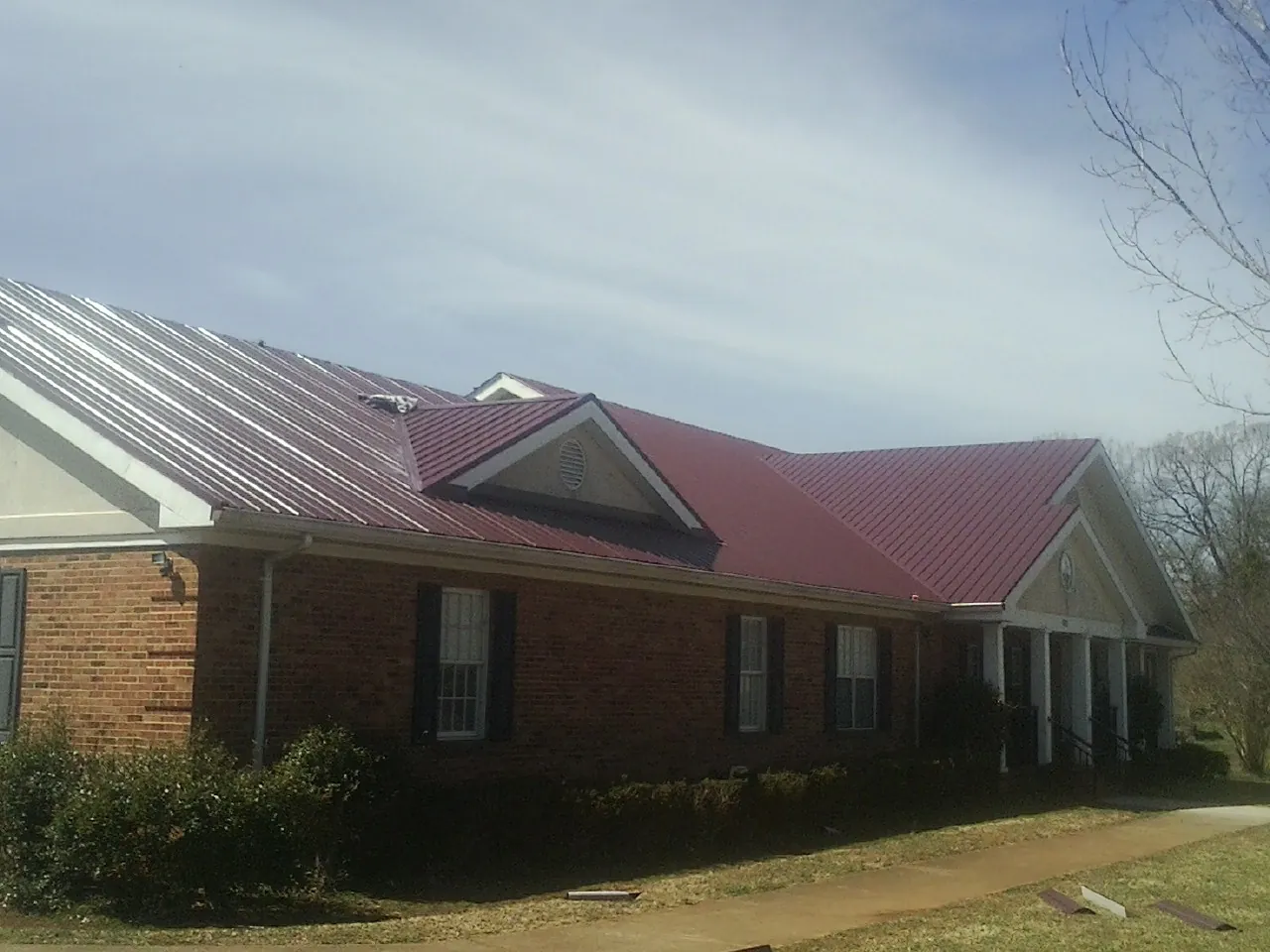 Red metal roof with gabled entries on a long brick building, from a Hail Damage Roof Repair job in Lacygne