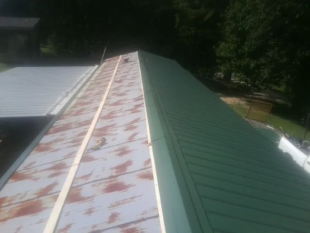 Old rusted panels beside newly installed green metal roofing — Wind Damage Roof Repair by Roofing Brothers in Lacygne