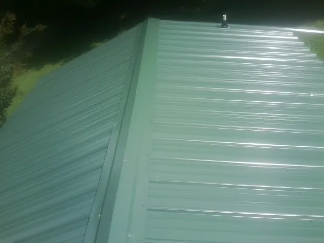 New green metal panels meeting at the ridge of a roof — Flat Roof Repair work by our crew in Lacygne