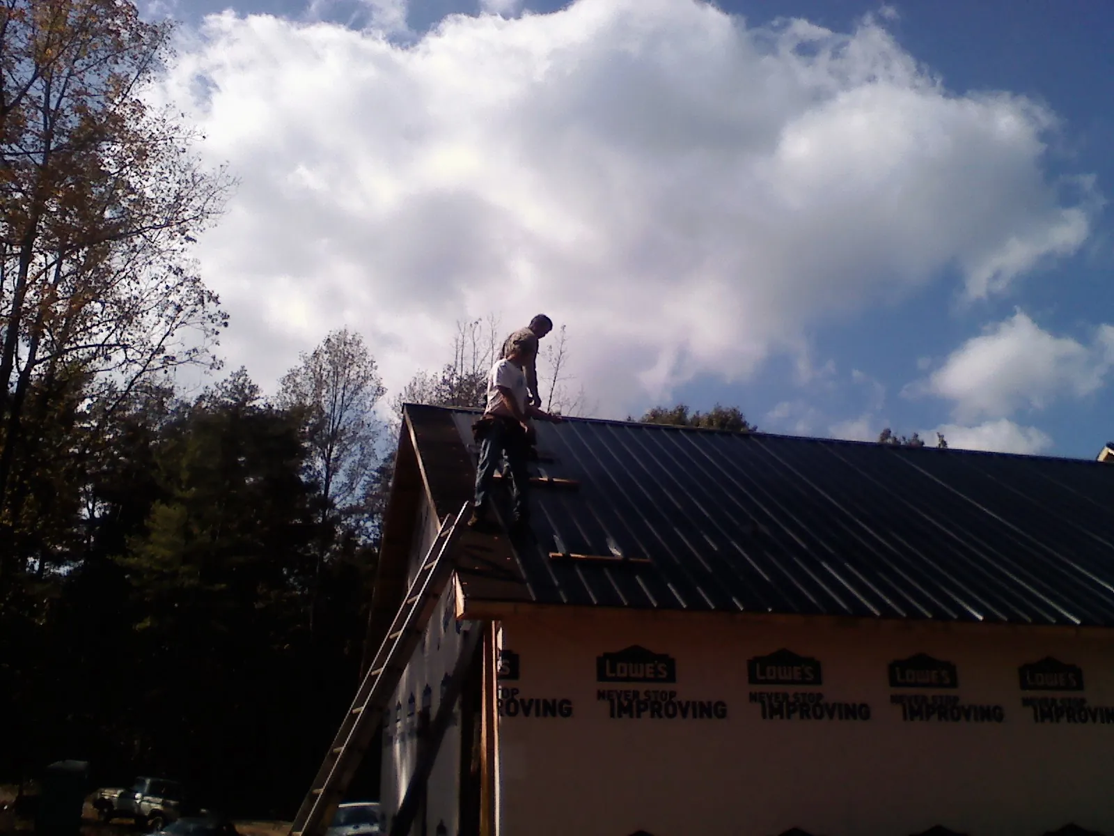 Roofer fastening dark metal panels high against a cloudy sky, from a Roof Inspection job in Lacygne