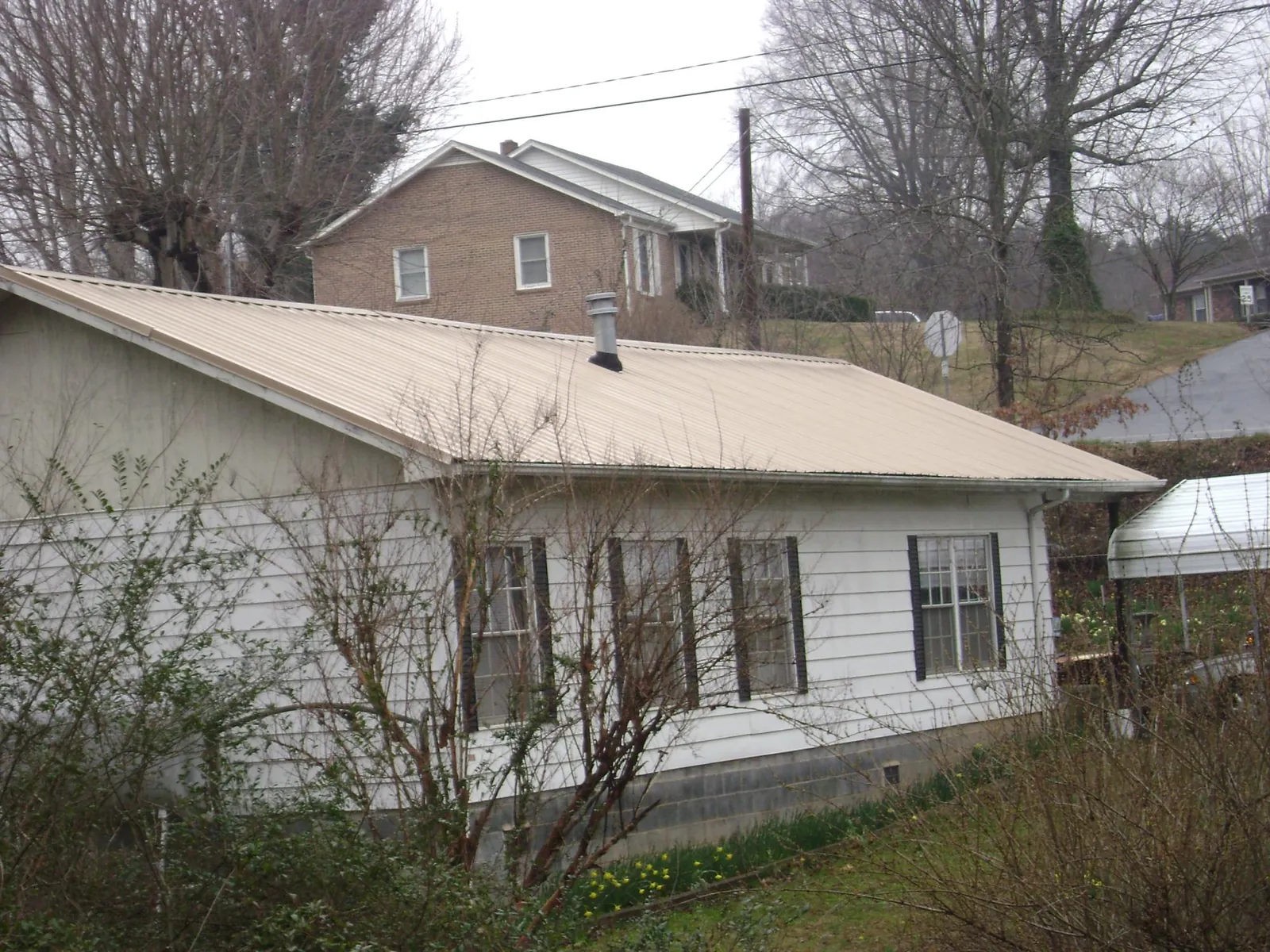 Tan metal roof on a white sided house set into a hillside — Commercial Roofing by Roofing Brothers in Lacygne