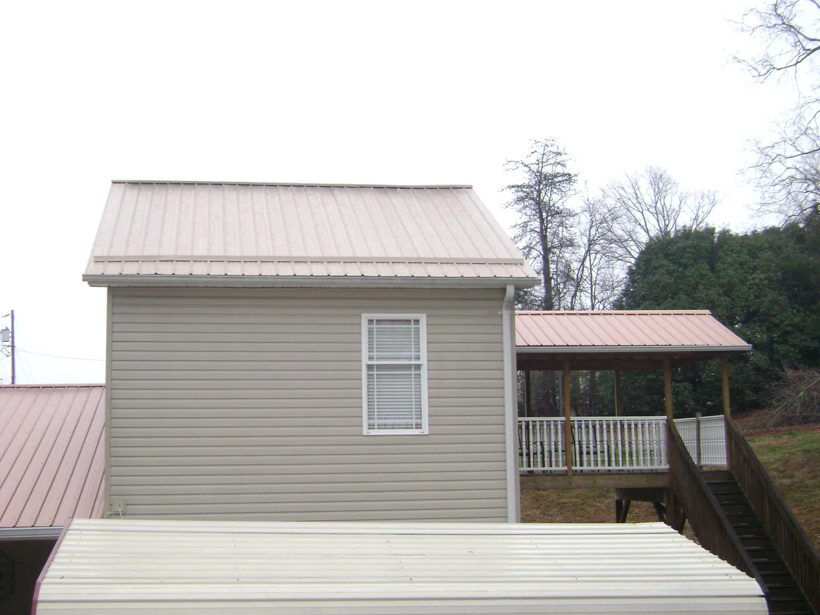 Tan metal roofs on a two story addition and attached porch, from a Roof Replacement job in Lacygne